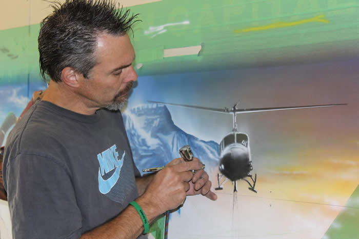 Greg Gislason peint à l'aérographe un hélicoptère sur une peinture murale